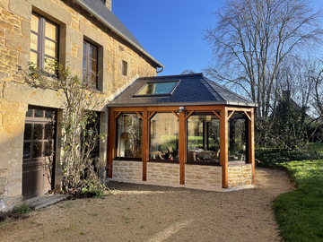 une véranda chaleureuse avec murets en pierres et poteaux bois brut travaillés