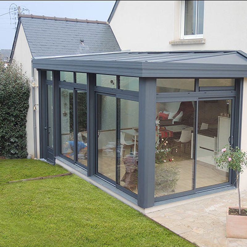 Véranda en aluminium gris anthracite avec toit plat, grandes baies vitrées coulissantes. Extension lumineuse donnant sur le jardin et la terrasse. Sapin de Noël visible.