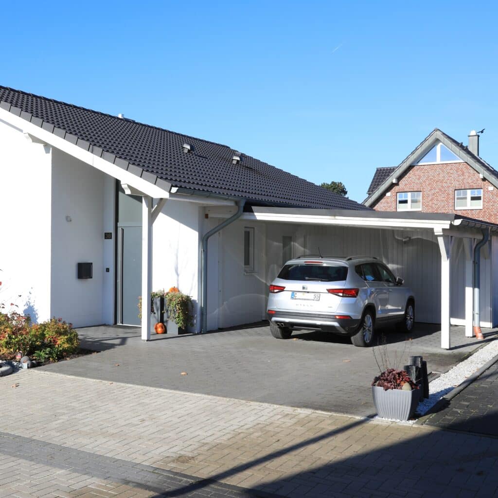 Maison moderne, carport et allée pavée de prestige Maison blanche contemporaine avec toit noir et carport intégré. Un SUV argenté est garé sur l'allée pavée (36).
