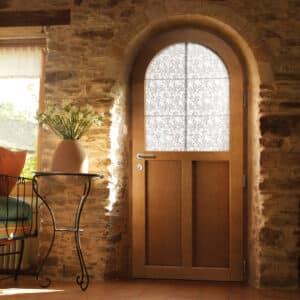 Porte en bois cintrée avec vitrage décoratif intégrée dans une épaisse arche de pierre rustique, éclairée par le soleil.